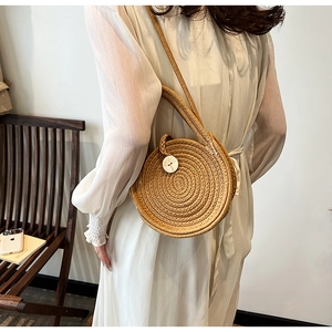 Outdoor lifestyle shot of a round woven straw crossbody bag with decorative white button