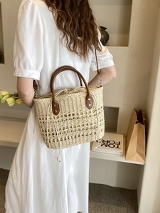 Detail of woven straw tote bag with brown leather handles worn by a model in white dress