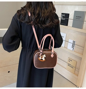 Detail of a brown PU leather crossbody bag featuring pink handles and a cute horse charm