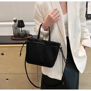 Detail of a black pleated PU leather crossbody bag with drawstring handle shown on a model