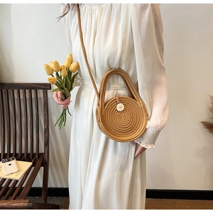 Detailed texture of circular straw woven bag with shoulder strap in a garden setting