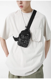 Détail du sac de poitrine en nylon noir avec motif graffiti de monstre blanc à l'avant