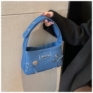 Détail du sac bandoulière en denim tendance avec bords effilochés et badges en métal