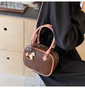Detail view of a vintage brown PU leather boston bag with pink edges and a horse charm