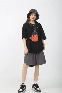 Front view of an orange and black crossbody bag worn with a stylish urban casual outfit