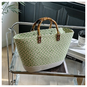 Green and white woven tote bag with natural bamboo handles on a modern shelf
