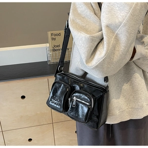 Close-up of the black glossy PU leather crossbody bag with dual front zipper pockets