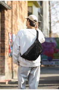 Homme portant un sac banane en nylon noir avec logo TIANDINGYU dans une rue en briques