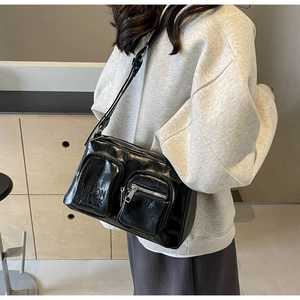 Detail of glossy black PU leather crossbody bag with multiple pockets and adjustable strap