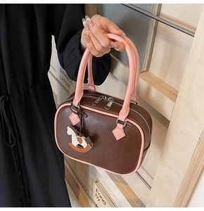 Detail of brown PU leather boston bag with pink handles and cute rocking horse charm