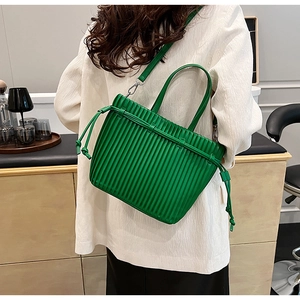 Detail of vibrant green pleated PU tote bag worn by a model in a minimalist setting