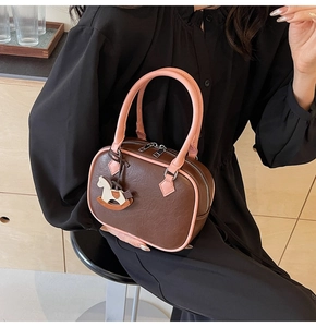 Close-up of brown pebbled leather handbag with pink handle and cute horse charm detail