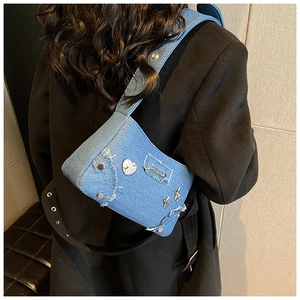 Détail du sac à bandoulière en denim avec clous étoiles et bords effilochés sur tissu bleu