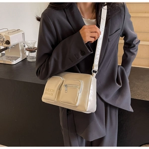 Detail of beige PU leather crossbody bag featuring two front pockets and brand logo