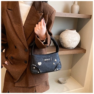 Détail du sac à bandoulière en denim gris avec cœurs et étoiles sur un manteau en laine