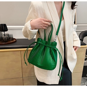 Detail of green pleated crossbody bucket bag with drawstring closure and leather strap