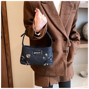 Détail du sac sous le bras en denim noir avec clous cœur et étoile en style Y2K