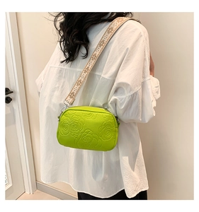 Detail showing bright green PU leather crossbody bag with rose embossing and wide strap