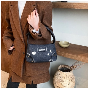 Détail du sac à main en denim noir avec clous en cœur argentés et franges sur modèle