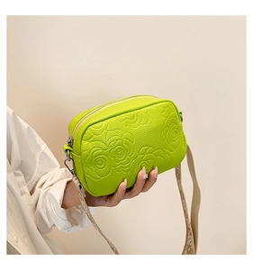 Detail of neon green PU leather crossbody bag featuring embossed floral patterns and strap