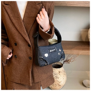 Détail du sac bandoulière en denim gris foncé avec clous en cœur et pompons à chaînes