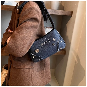 Détail du sac bandoulière en denim bleu foncé avec clous cœur argentés et bords effilochés