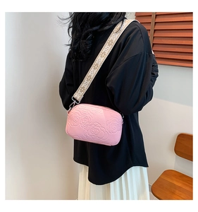 Detail of pink PU leather crossbody bag featuring 3D rose embossing and ethnic woven strap