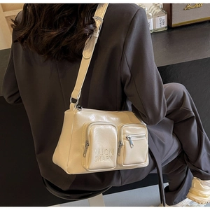 Detail of beige faux leather crossbody bag showing dual exterior zippers and brand text