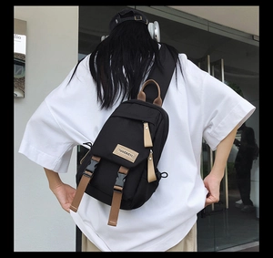 Rear view of black nylon crossbody sling bag with buckle and brown strap on a model