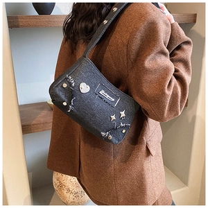 Détail du sac bandoulière en denim gris foncé avec clous en cœur et bords effilochés