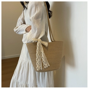 Detailed close-up of woven straw shoulder bag with elegant white lace ribbon trim