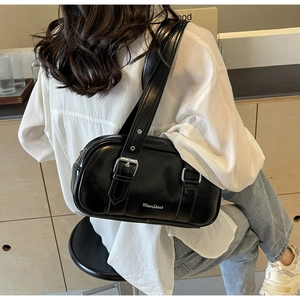 Side view of a black glossy PU leather underarm bag worn by a model in a warm interior