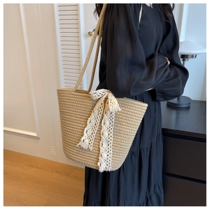 Detail of handwoven beige tote bag featuring delicate white lace bow and rope handles