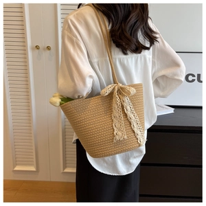 Detail of hand-woven straw shoulder bag featuring a white lace bow and floral accent