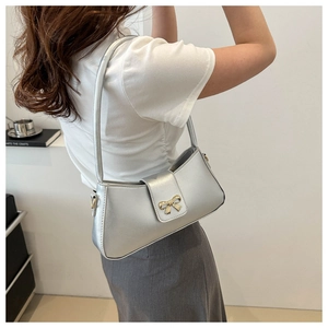 Sac baguette en cuir argenté avec fermoir nœud doré porté par un mannequin en tenue chic