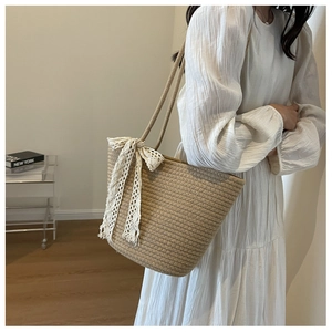 Close-up of a woven tote bag featuring a decorative white lace bow and natural khaki texture