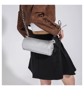 Detail of silver cylindrical PU leather bag with metallic chain strap worn by a model