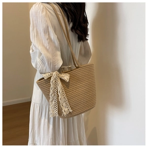 Detail of light brown woven tote bag featuring a white lace bow on the side for women