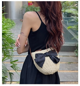 Sac bandoulière en paille tressée avec grand nœud noir sur fond de jardin naturel