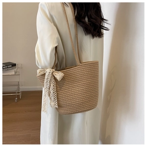 Detail of hand-woven straw tote bag with white crochet lace bow and slim shoulder straps