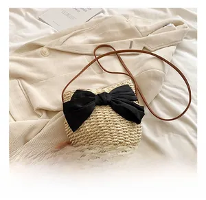Détail d'un sac bandoulière en paille avec un grand nœud en satin noir et une bandoulière