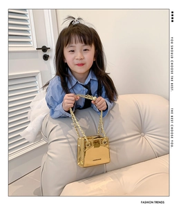 Close-up of a metallic gold mini handbag with a chain strap held by a model on a sofa