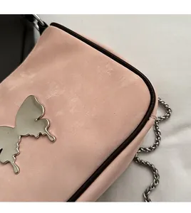 Détail du sac à bandoulière en velours rose avec un grand papillon en métal argenté