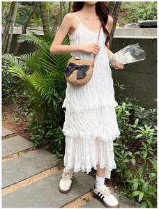 Détail d'un sac bandoulière en paille avec nœud noir sur une robe d'été blanche