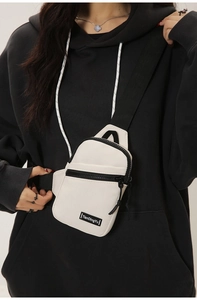 Close-up of cream nylon crossbody chest bag with black zippers and woven strap