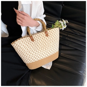 Detail of woven tote bag with natural bamboo handles and contrast leather stitching