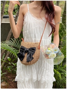 Détail du sac bandoulière en paille avec grand nœud en satin noir sur robe en dentelle