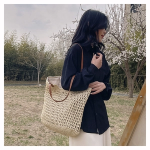 Outdoor side view of a large woven tote bag in cream mesh with brown leather straps