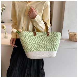 Detail of woven green and white herringbone tote bag featuring natural bamboo top handles