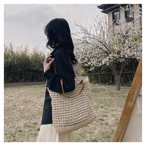 Close-up of handwoven hollow straw tote bag with brown leather handles in outdoor garden